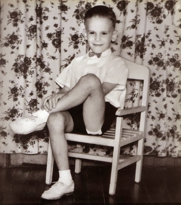 Luis Alberto Spinetta de niño, sentado en una silla en una foto blanco y negro, sonriendo.